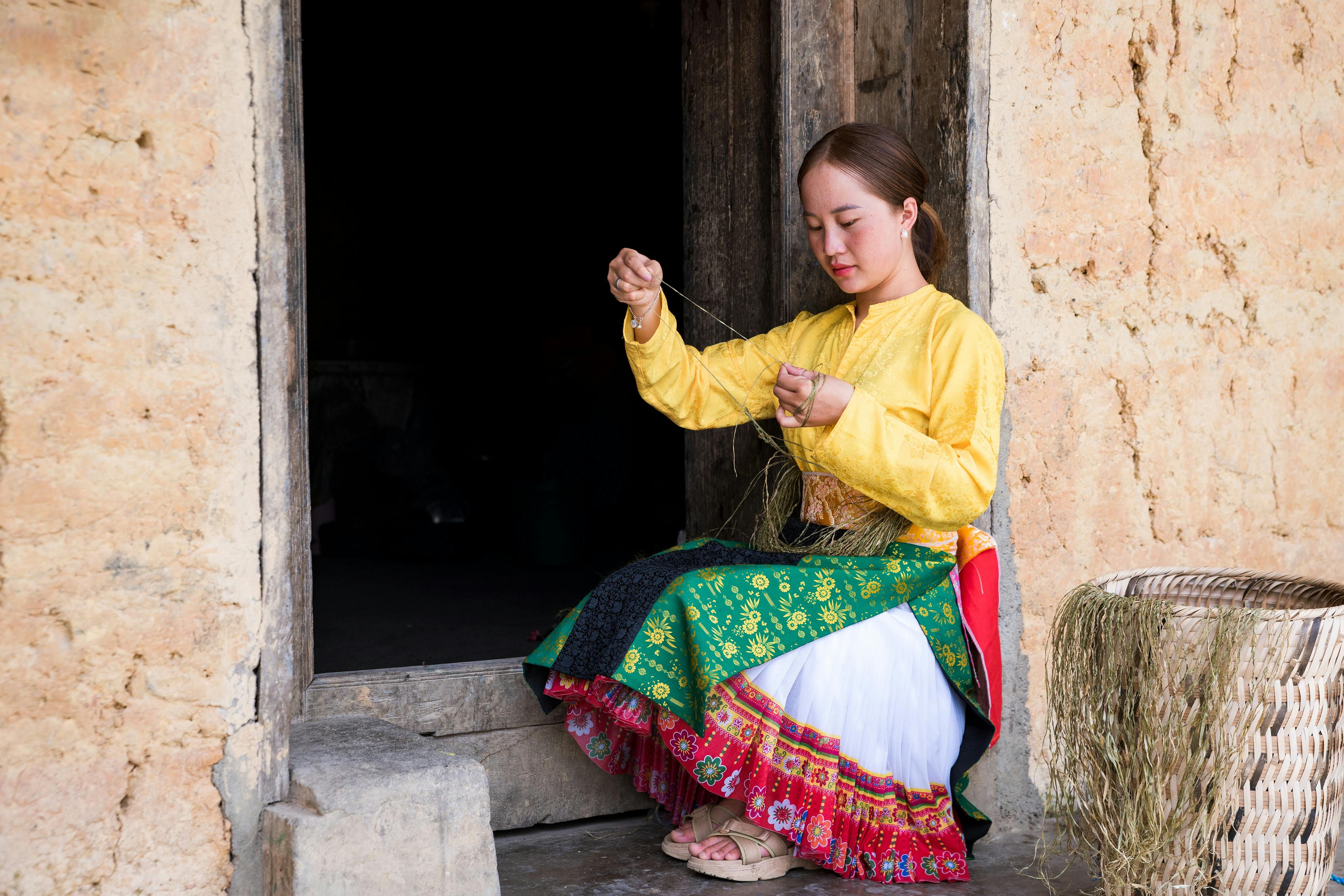 A woman in traditional attire weaving outdoors, showcasing cultural heritage and craftsmanship.