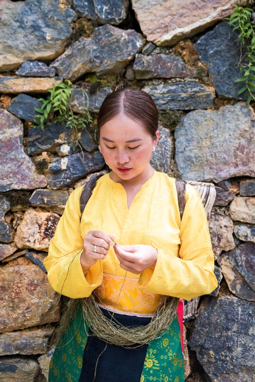 Free Woman in traditional attire crafting against a rustic stone wall outdoors. Stock Photo