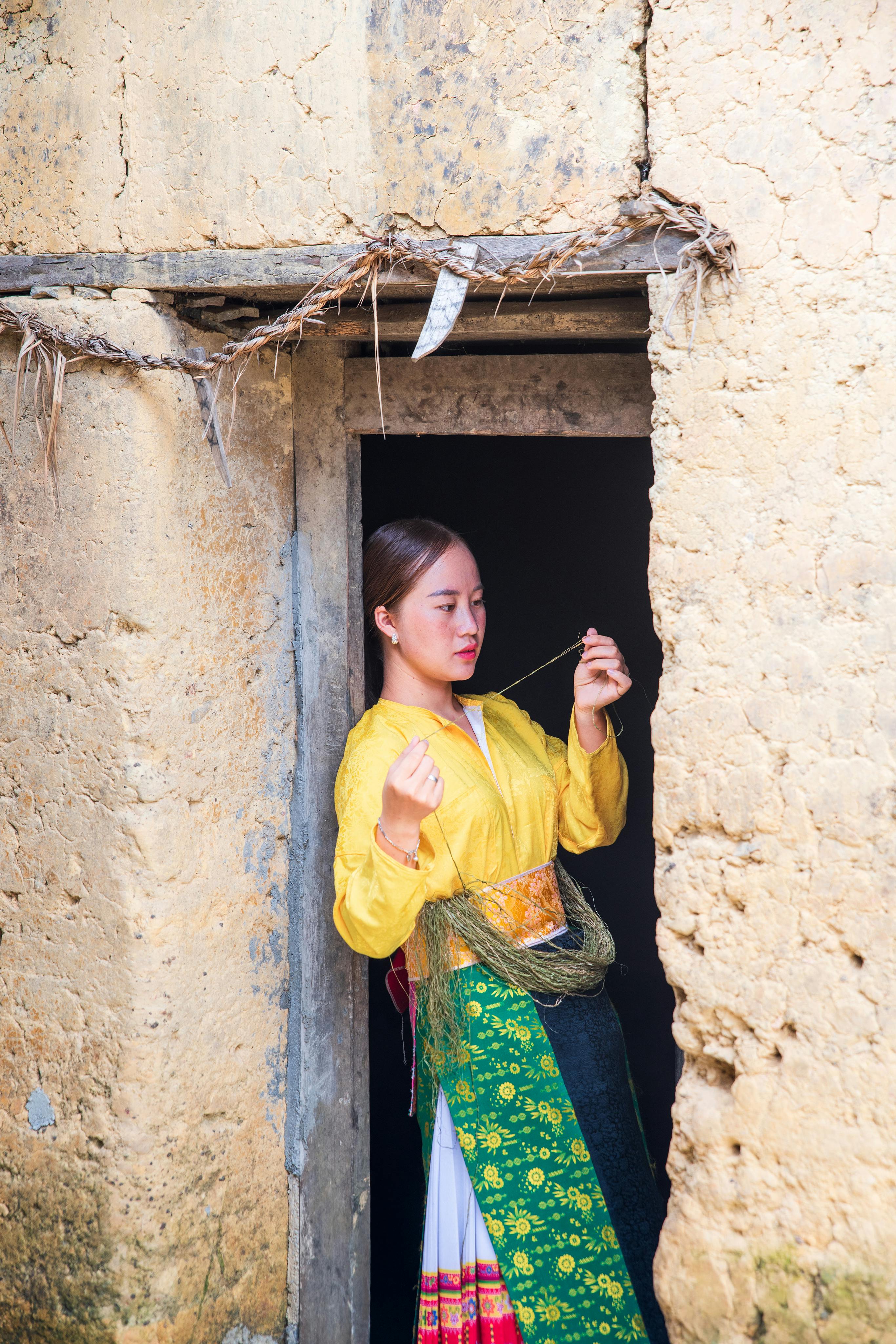A woman in vibrant traditional attire stands in a rustic doorway, showcasing cultural fashion.