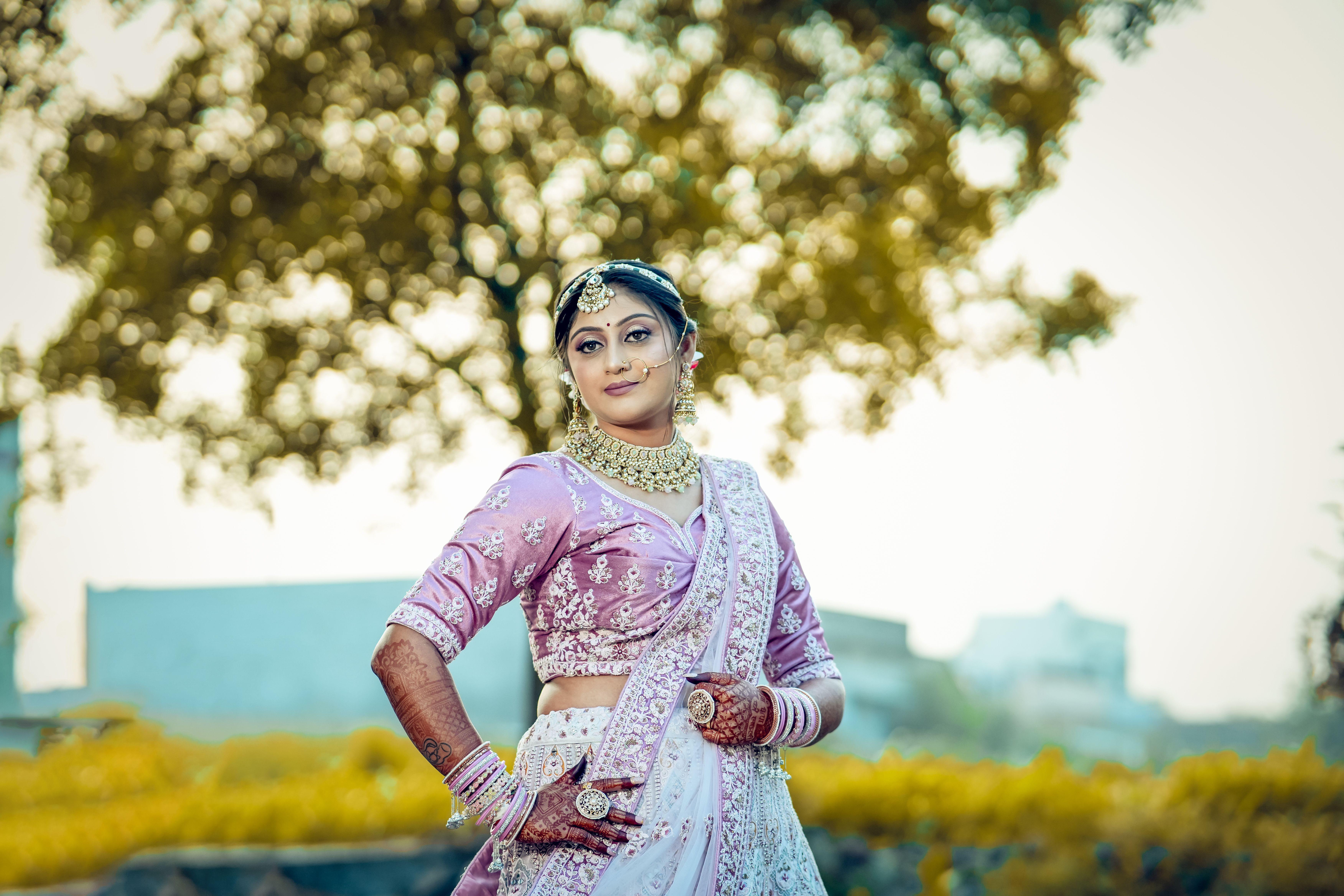 A beautiful bride in traditional Indian attire poses gracefully outdoors, exuding elegance and charm.