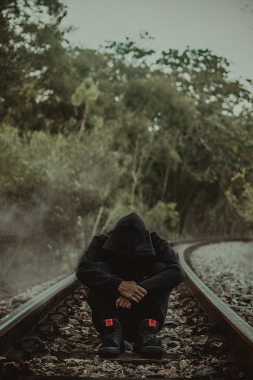 Photo of Man Sitting Alone in the Middle of a Train Track