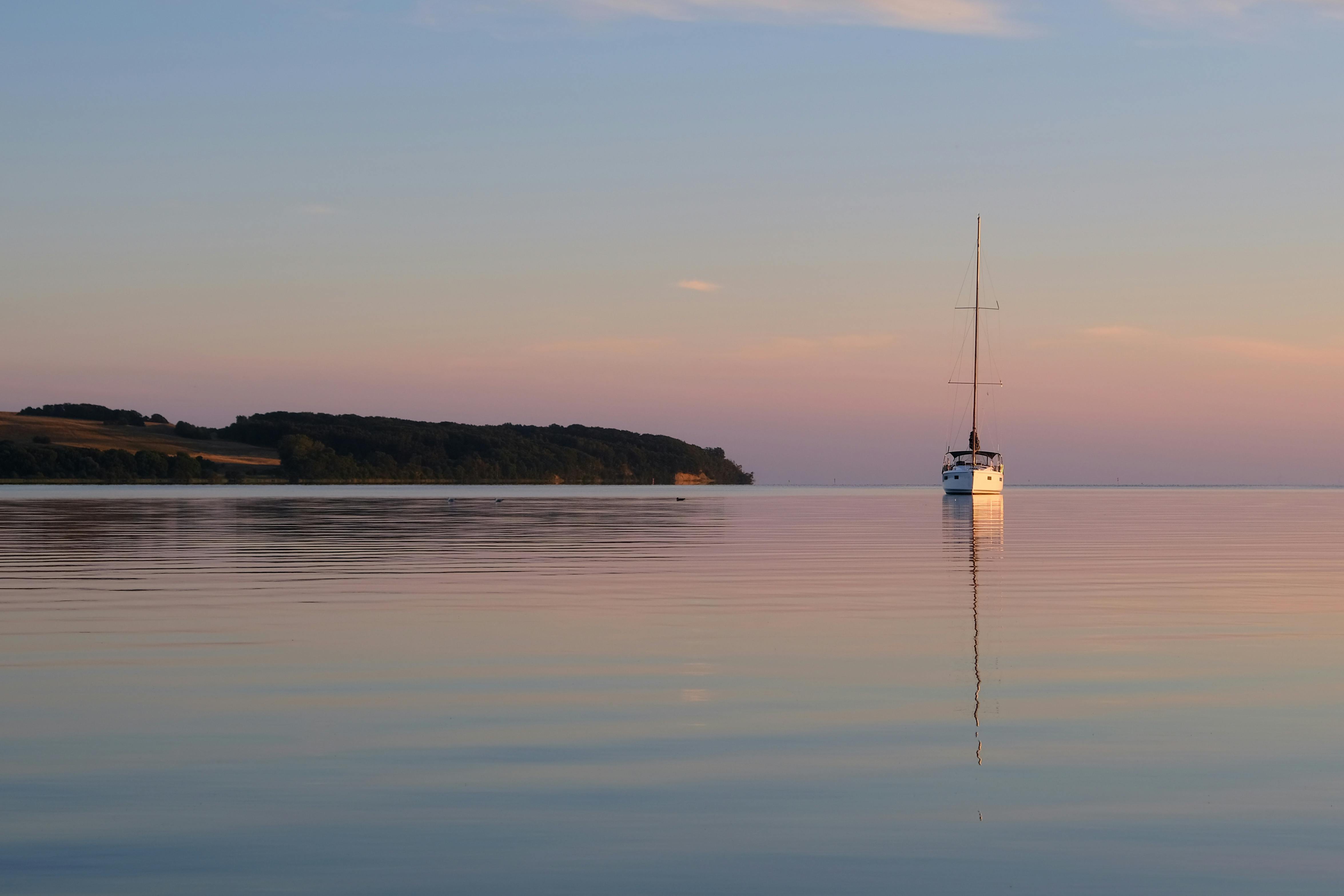 A calm ocean horizon at sunset with a single boat in the distance