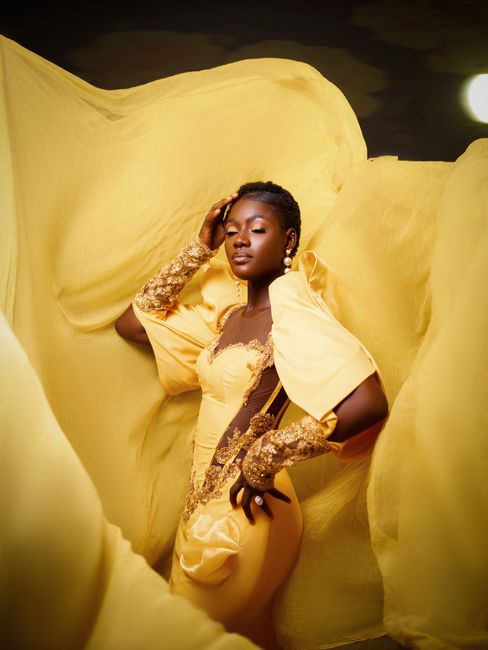 Elegant portrait of a black woman in a yellow dress with a flowing fabric background, embodying high fashion.
