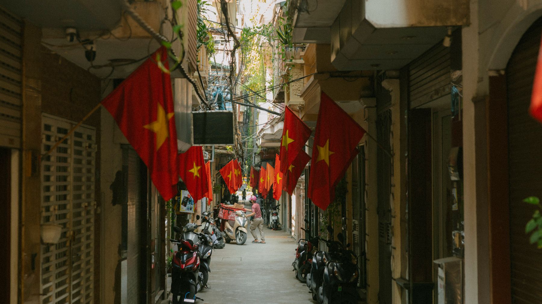 A narrow street adorned with red Vietnamese flags alongside parked scooters, reflecting urban life in Vietnam.