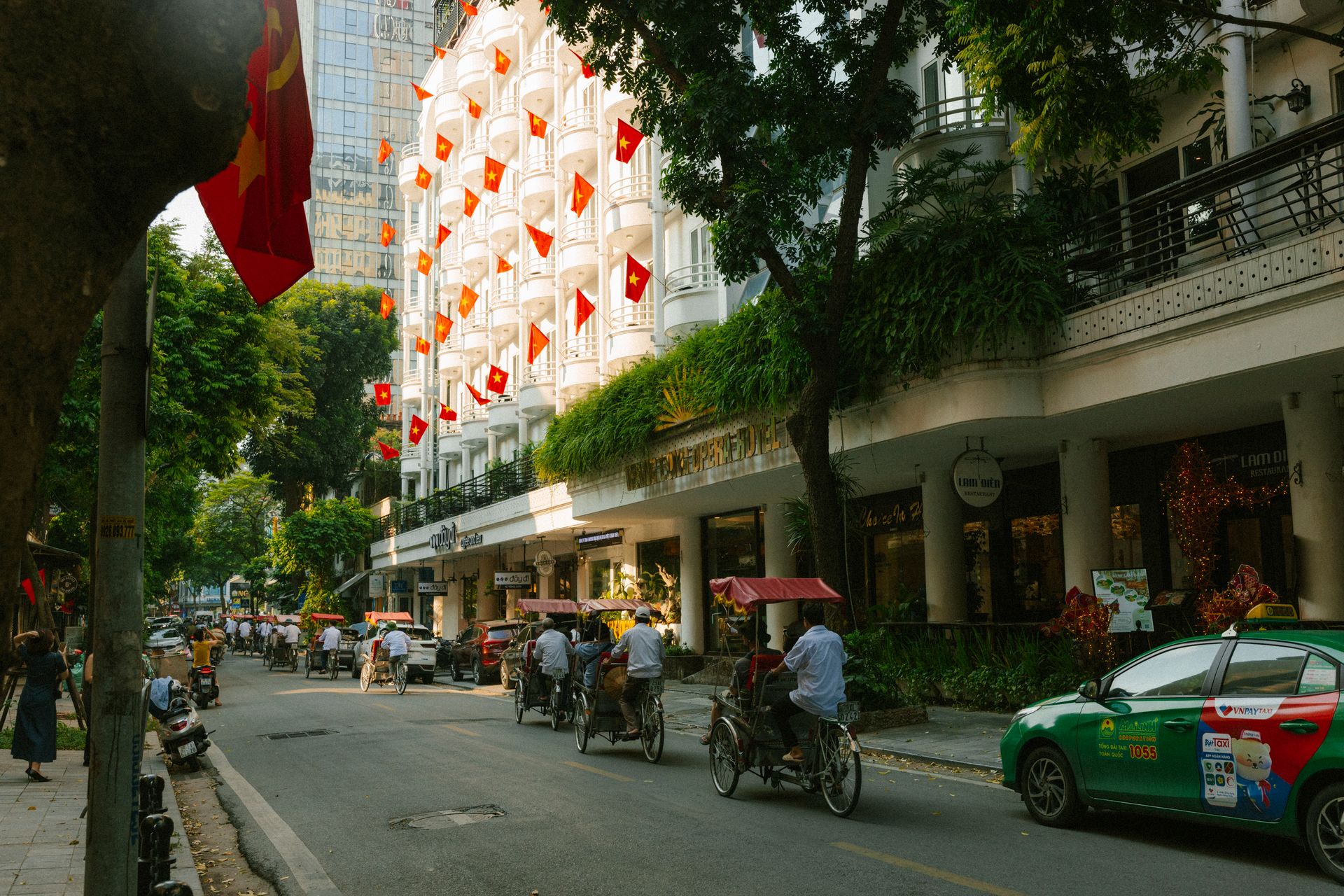 A lively Hanoi street with flags, bicycles, and greenery. Captures urban Vietnamese life.
