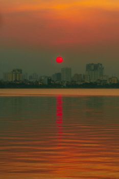 A mesmerizing sunset with vibrant colors over a city skyline and its reflection on calm waters.