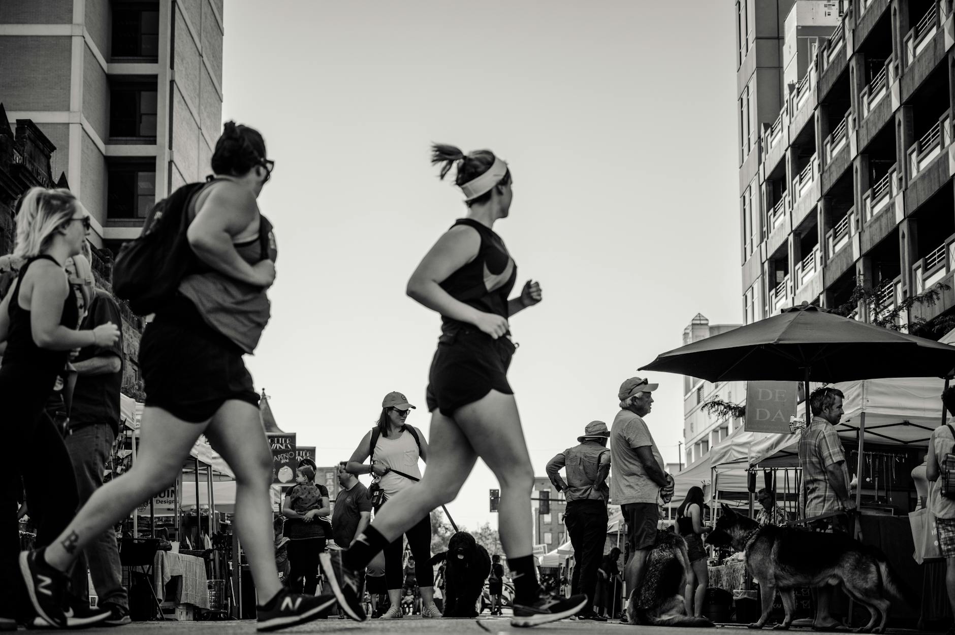 Black and white photo of people jogging and walking in a lively city street.