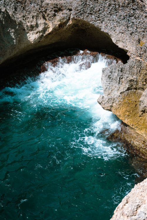 Free Vibrant ocean waves crashing against a rocky arch, showcasing natural beauty. Stock Photo