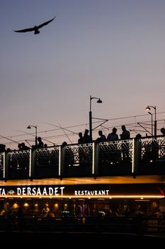 Silhouettes on a bridge at sunset above a lively restaurant scene.