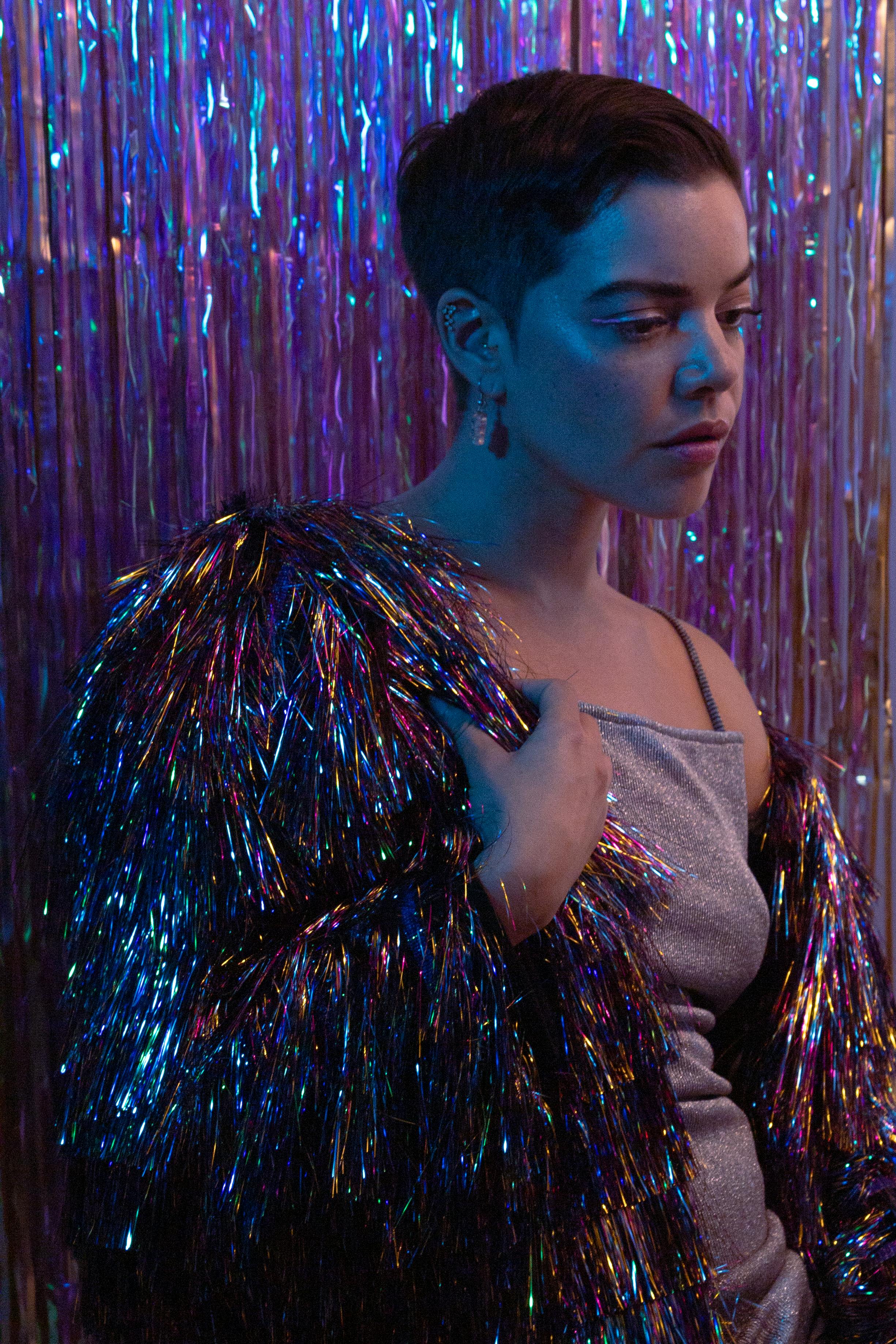 A stylish woman in a glittery outfit amidst a metallic backdrop, exuding glamor.