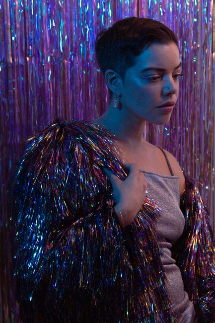 A stylish woman in a glittery outfit amidst a metallic backdrop, exuding glamor.