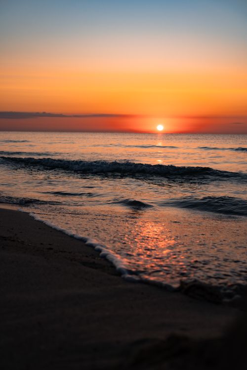 Free Beautiful sunset over the ocean with vibrant colors reflecting on the water and sandy beach. Stock Photo