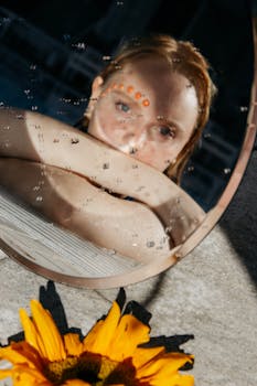 一张创意照片中，湿镜子映出向日葵旁的一位女士，唤起了一种宁静的心情