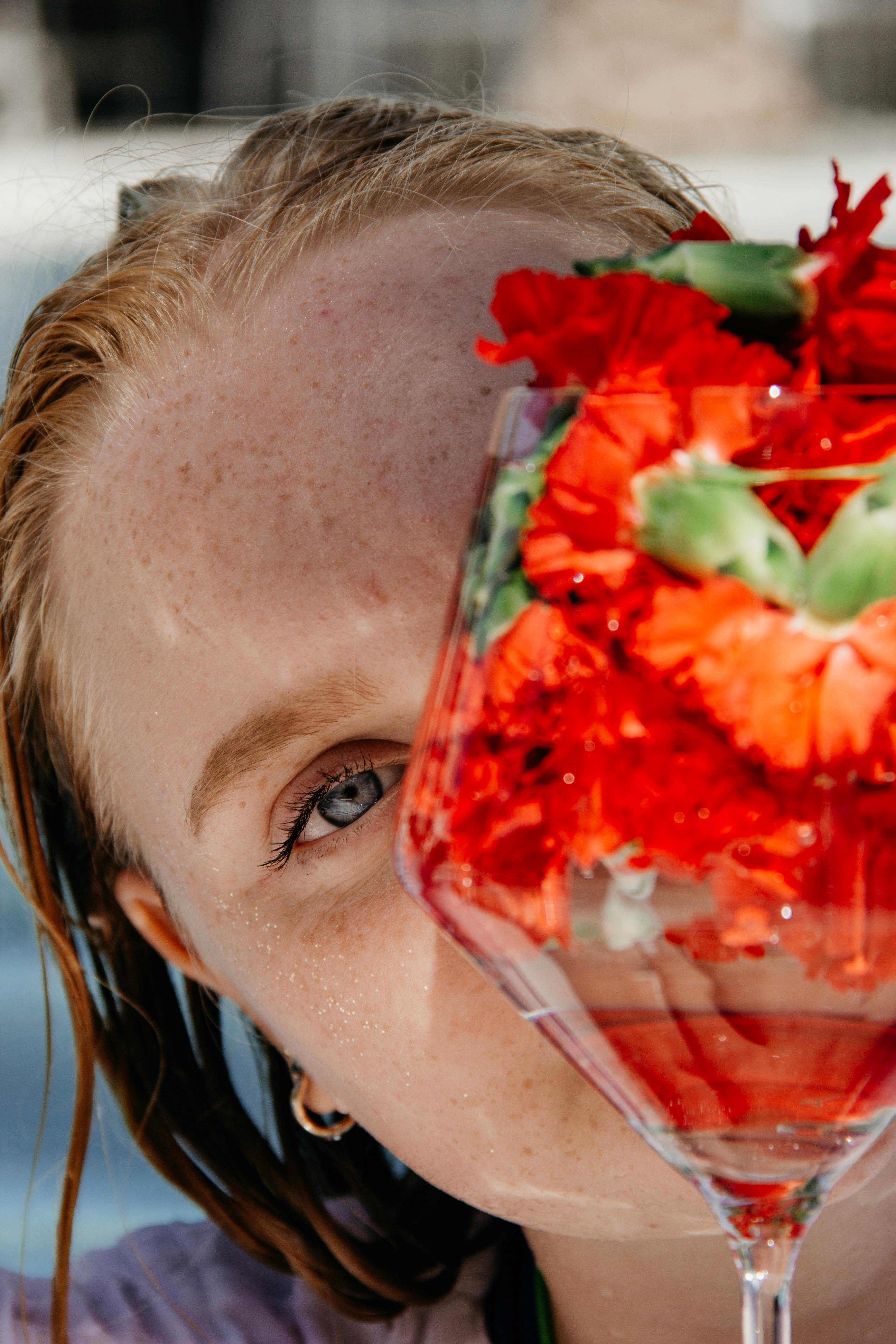 Close-up of a woman with red flowers in a glass, highlighting her eye by the poolside.
