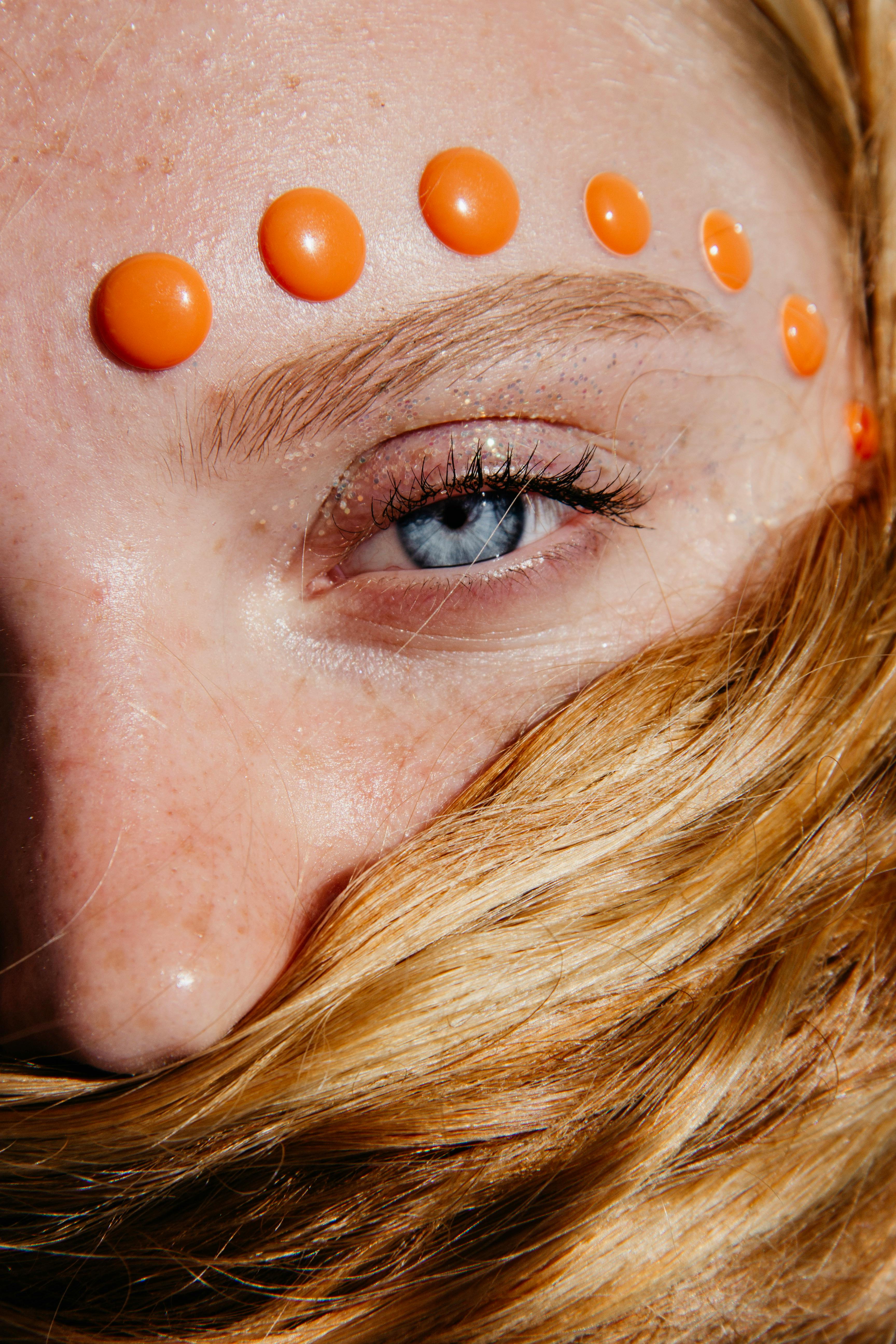 A creative close-up of a woman's eye embellished with orange beads, highlighting artistic expression.