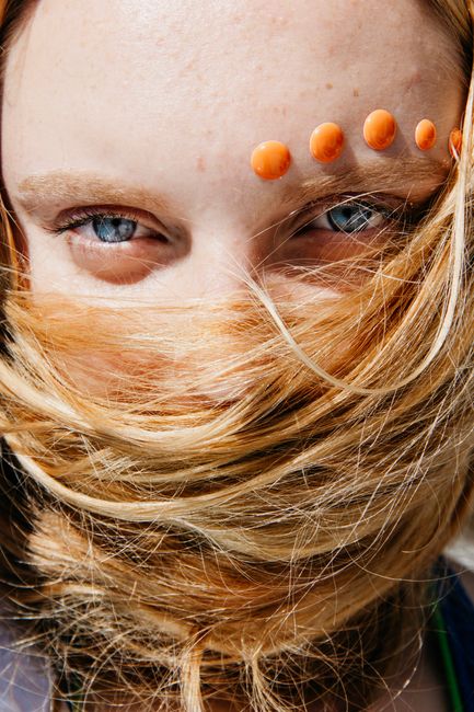 Close-up of a woman with blue eyes, hair over her face, and orange stickers.