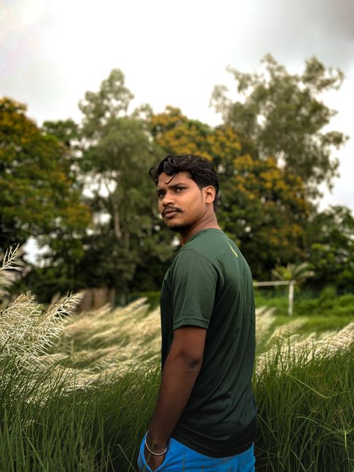 Free Outdoor portrait of a man standing in a green field with lush trees in background. Stock Photo