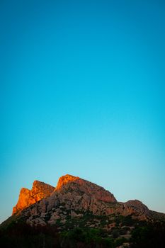 Vibrant orange sunset lighting up rocky mountain peaks under a clear blue sky.