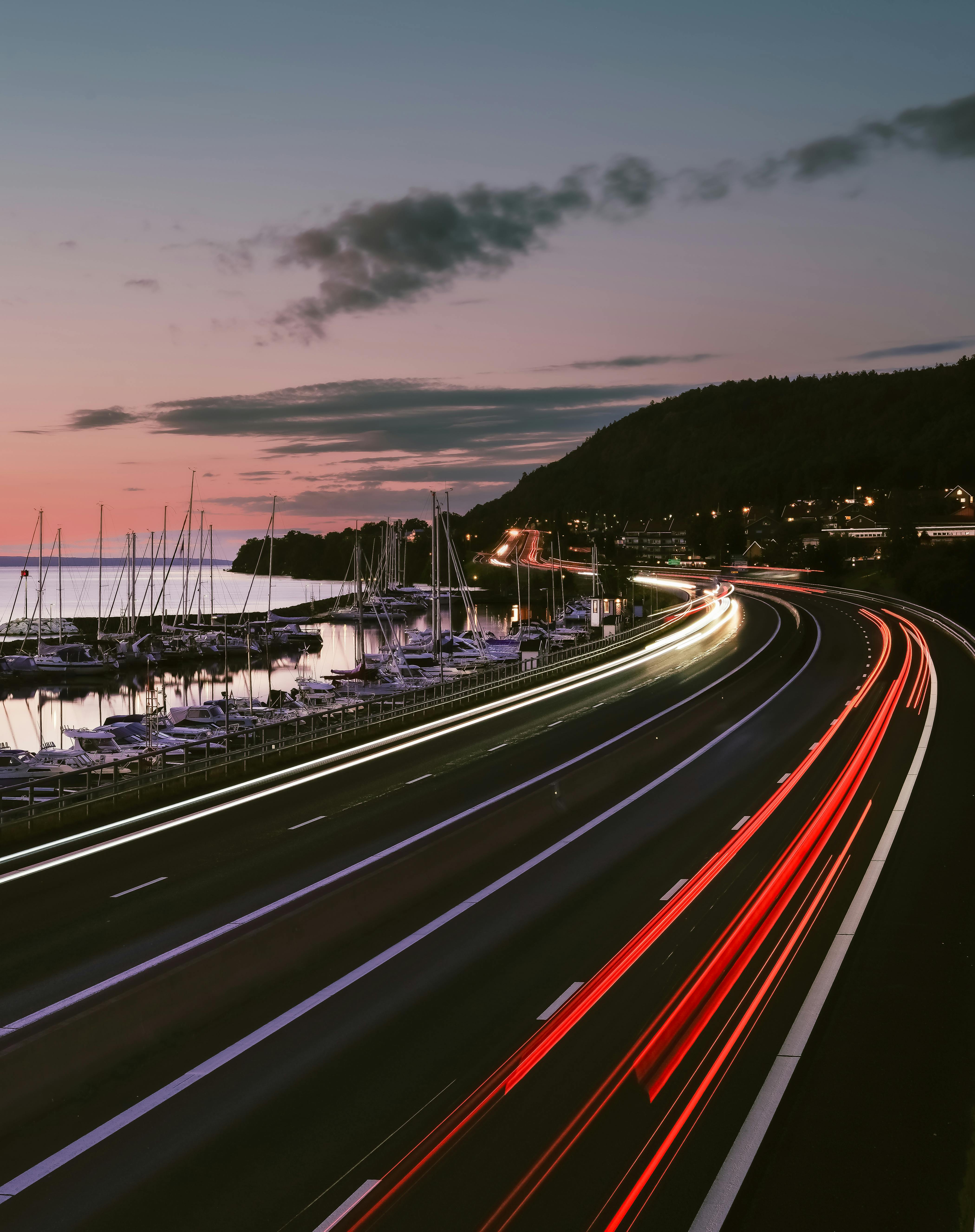 Highway at dusk with light trails and marina, capturing fast-paced travel.