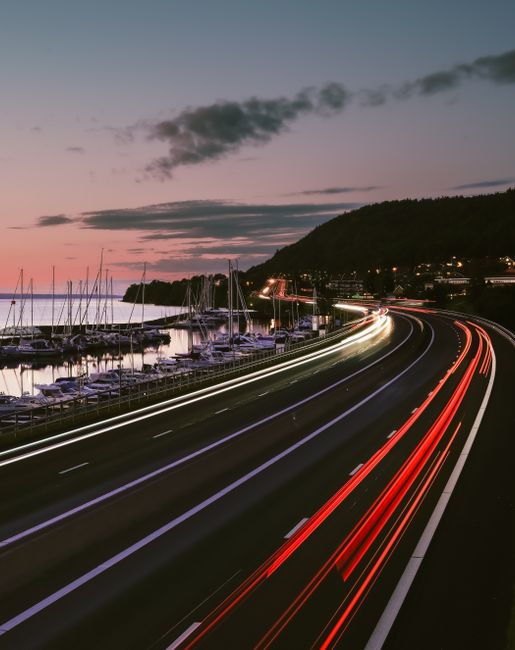 Highway at dusk with light trails and marina, capturing fast-paced travel.