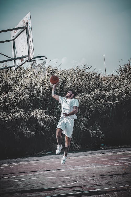 Man Wearing White Shirt Jumps in Front of Basketball Ring