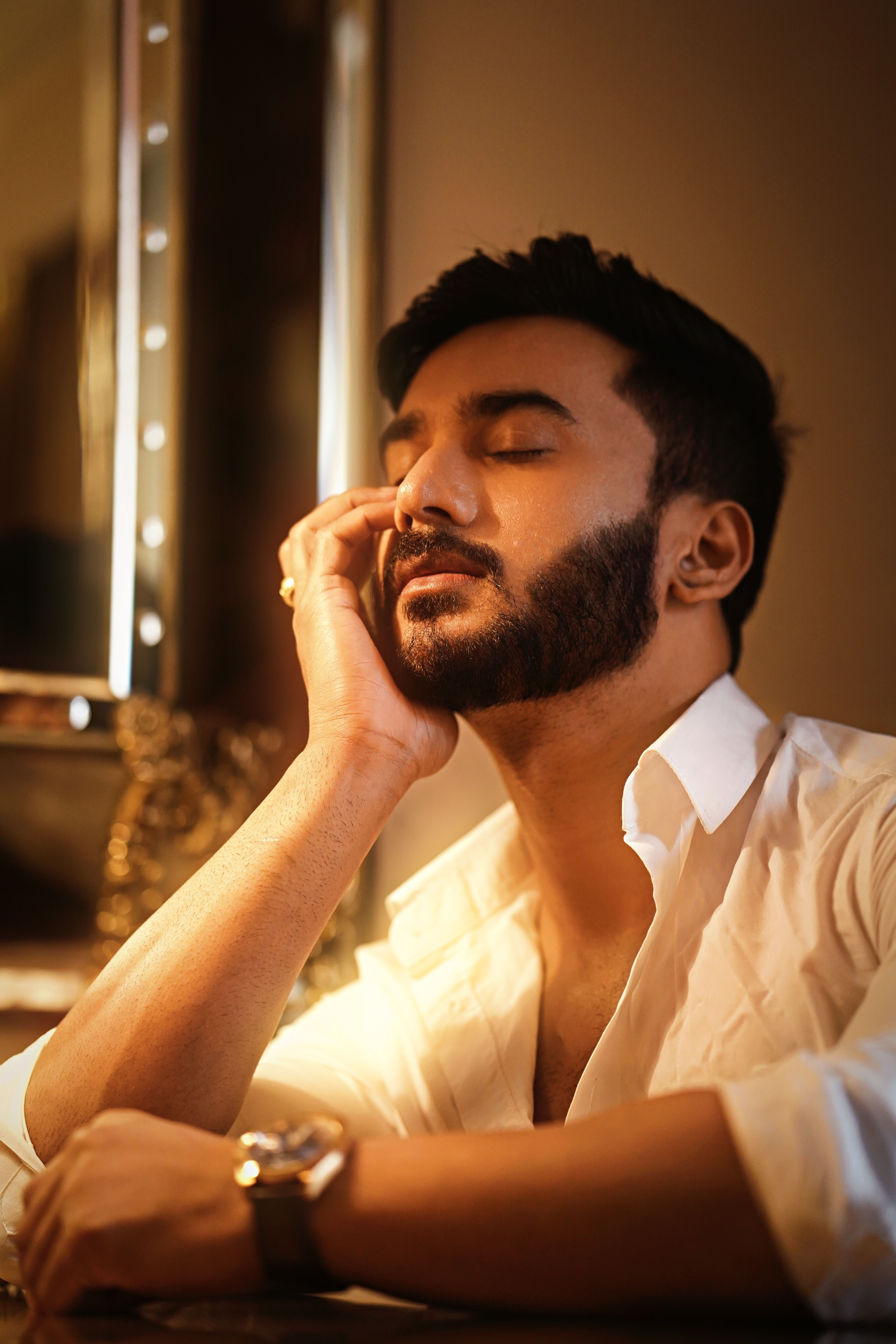 Fashion portrait of a bearded man in a white shirt with closed eyes, exuding calm.