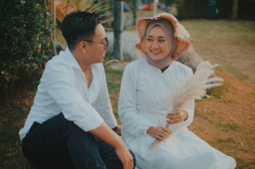 Femme Vêtue D'une Robe à Manches Longues Blanche Tenant Une Fleur Blanche Assise à Côté De L'homme Portant Une Chemise De Ville Blanche Et Un Pantalon Noir