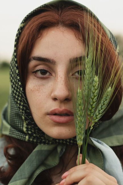 Close-up of a woman with red hair and green headscarf holding wheat stalks in Qazvin, Iran.
