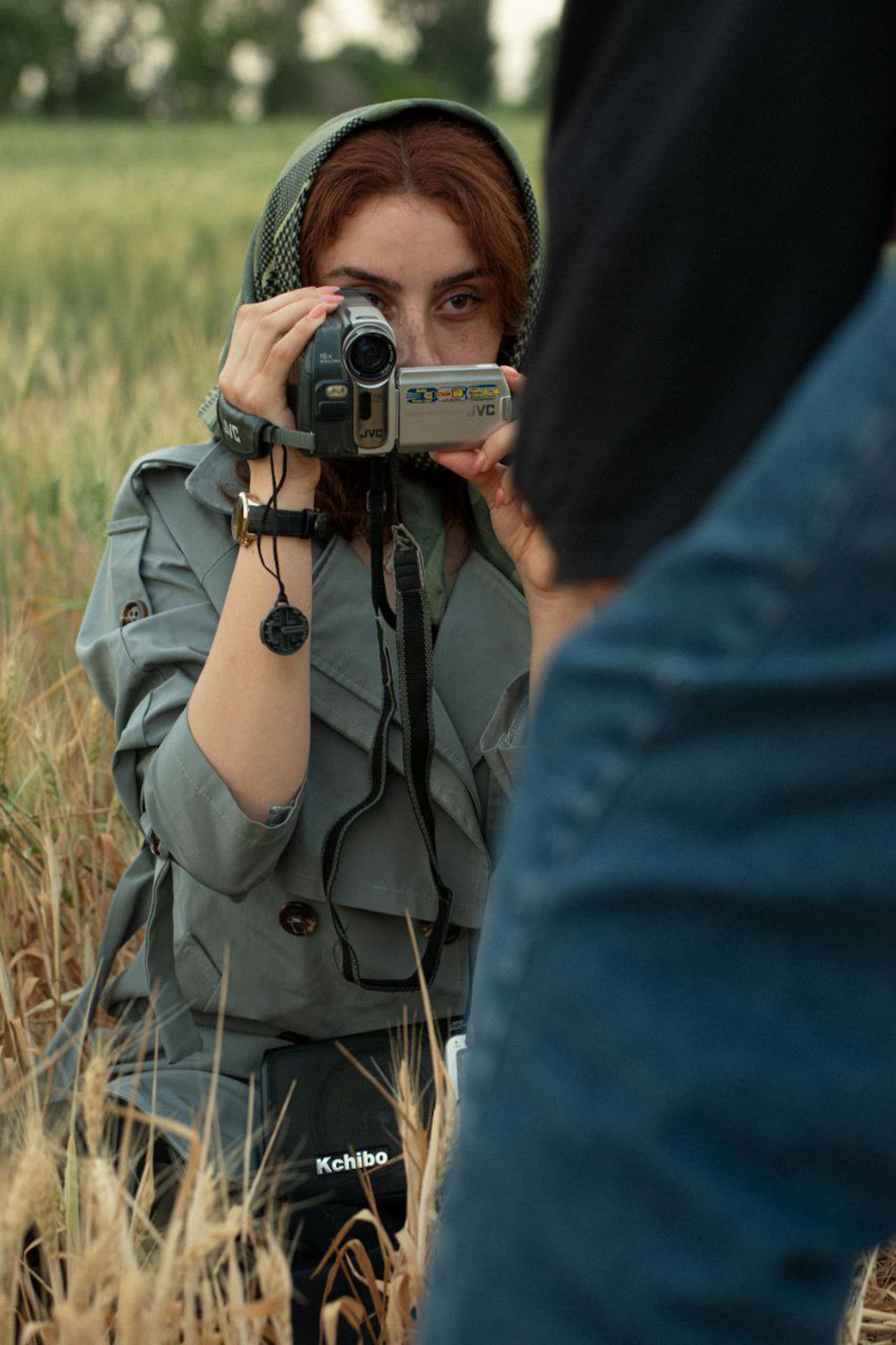 Woman holding a vintage camera, filming in a field, depicting outdoor leisure and creativity.