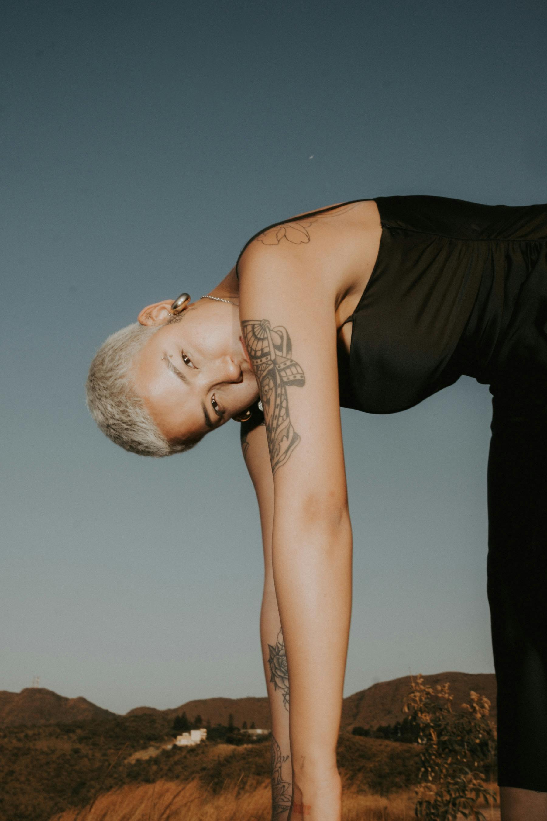 A fashion-forward woman with tattoos poses uniquely against a scenic Brazilian landscape.