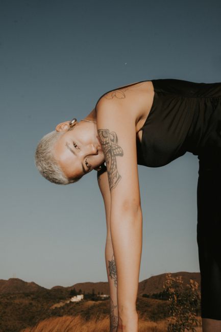 A fashion-forward woman with tattoos poses uniquely against a scenic Brazilian landscape.
