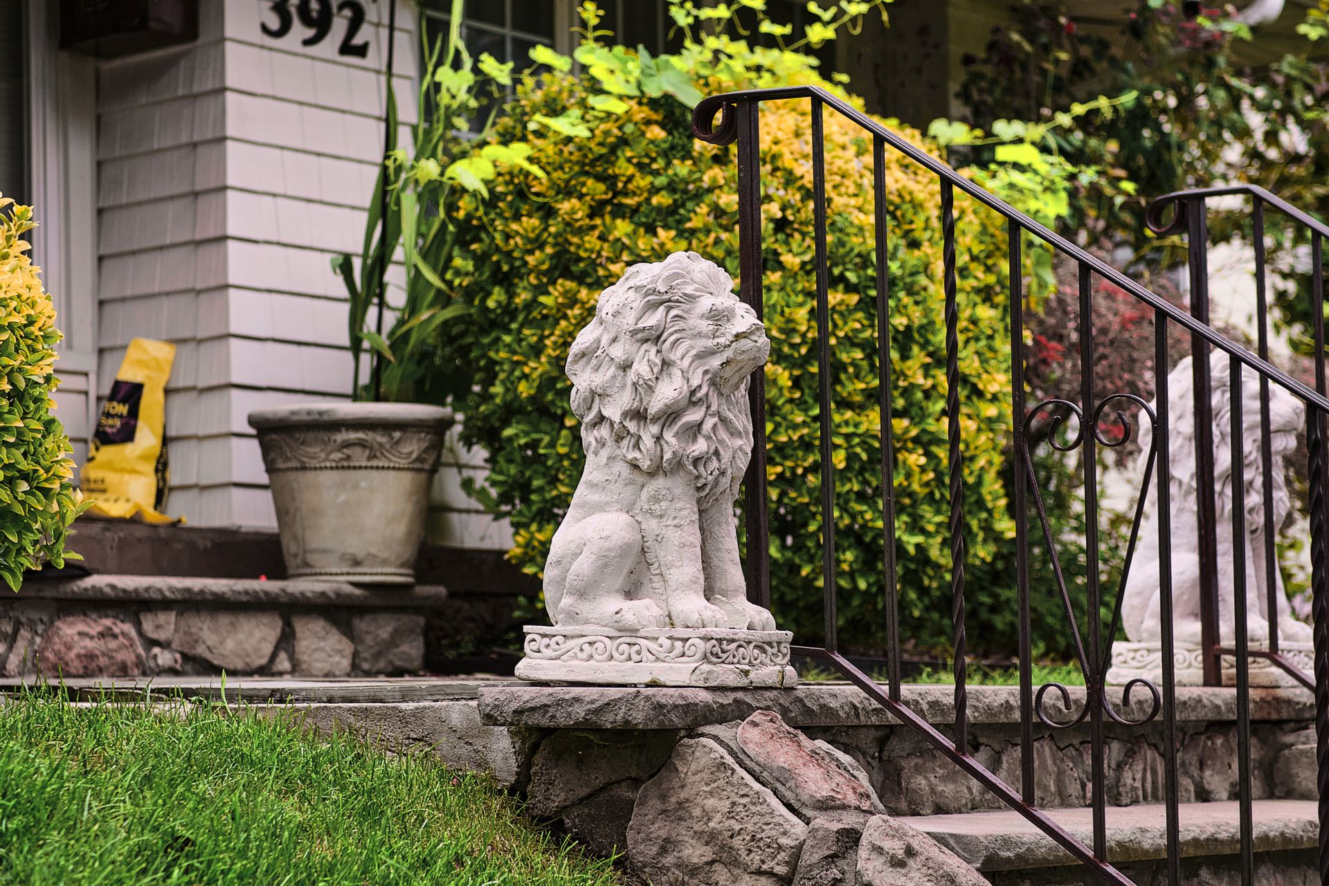 A decorative stone lion statue ornaments a vibrant garden entrance, enhancing the home's curb appeal.