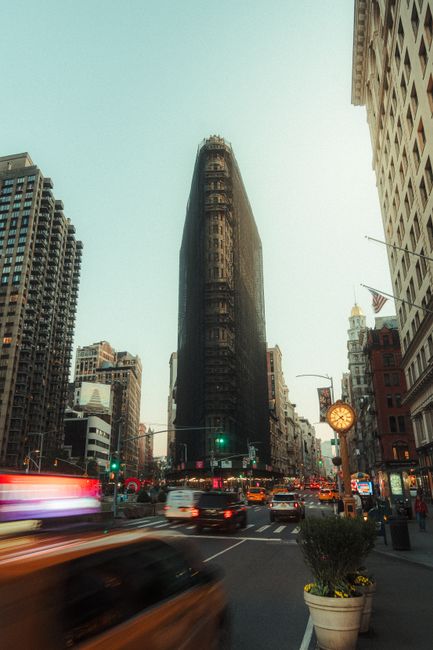 Street view of the Flatiron Building in NYC with vibrant traffic light trails at dusk.