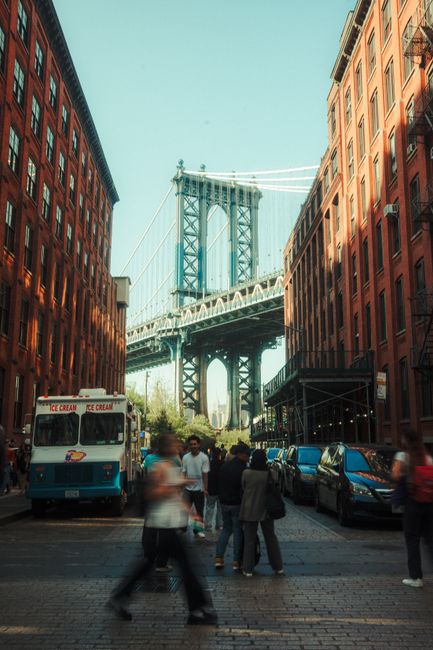 A bustling street scene in Dumbo, Brooklyn with the Manhattan Bridge in the background.