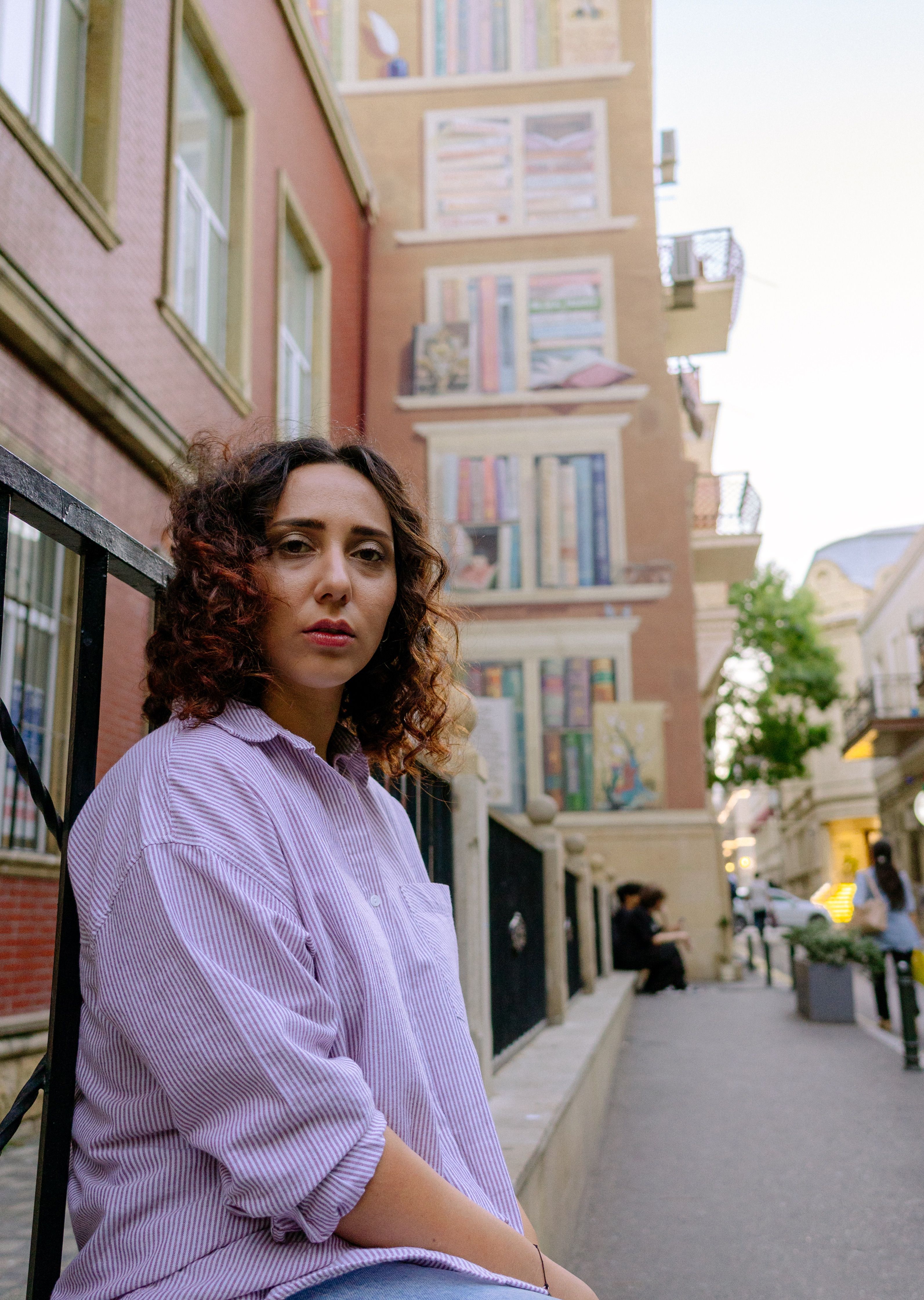 Casual portrait of a woman sitting in a city street with an artistic backdrop.