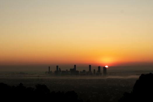 Stunning sunrise over Brisbane skyline with mist, capturing a warm, serene atmosphere.