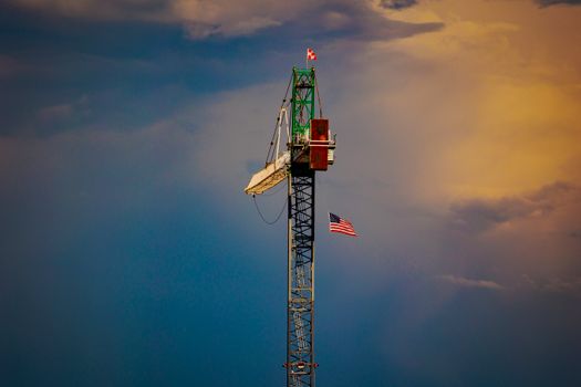 A tower crane with an American flag against a dramatic sunset sky in Mesa, AZ.
