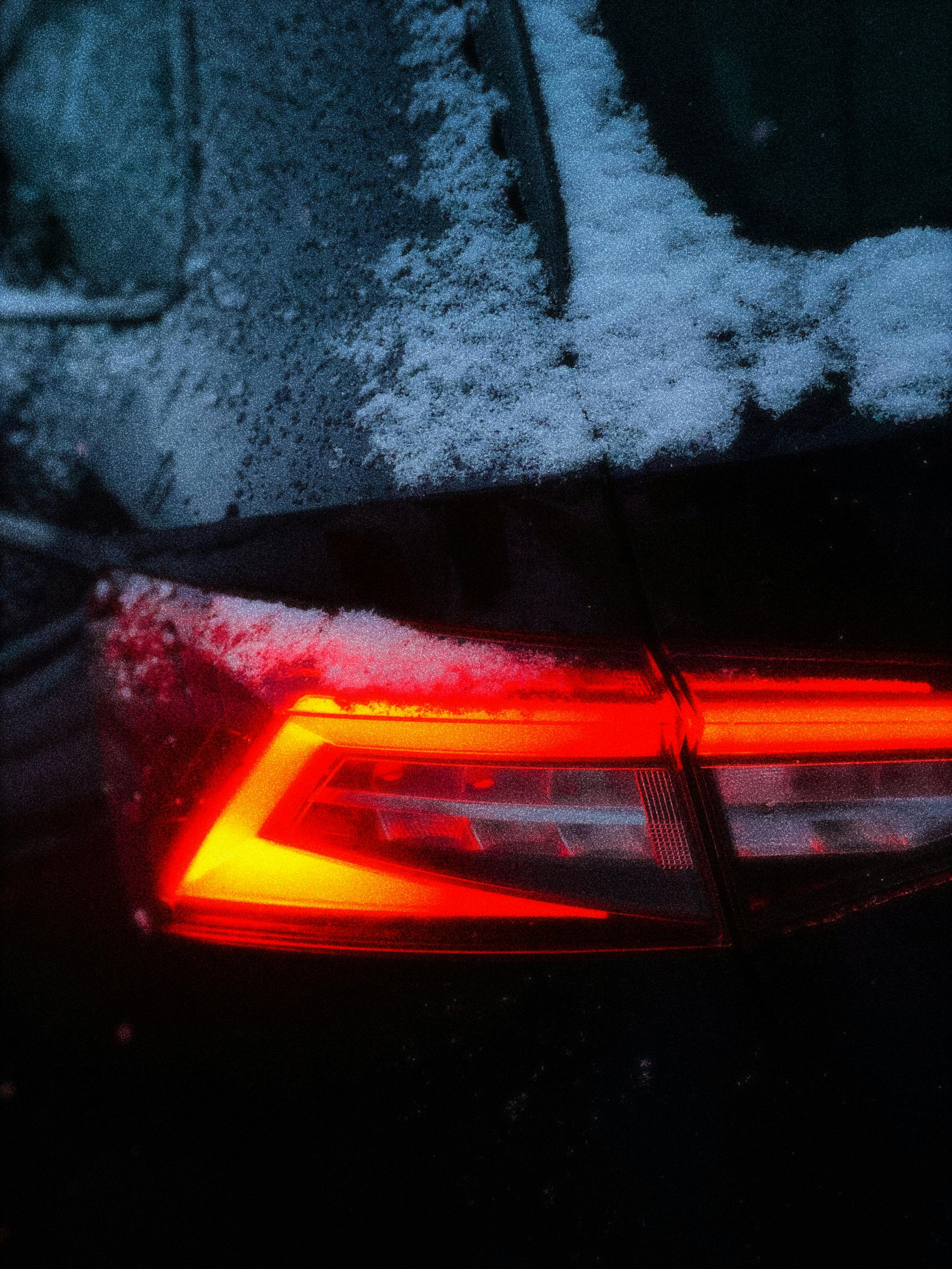 Car with bright red tail light in snowy urban setting, a classic winter scene.