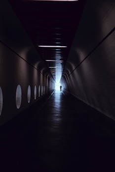 一个孤独的剪影穿过黑暗隧道，隧道壁上有一扇圆形窗户，营造出一种怪异的氛围