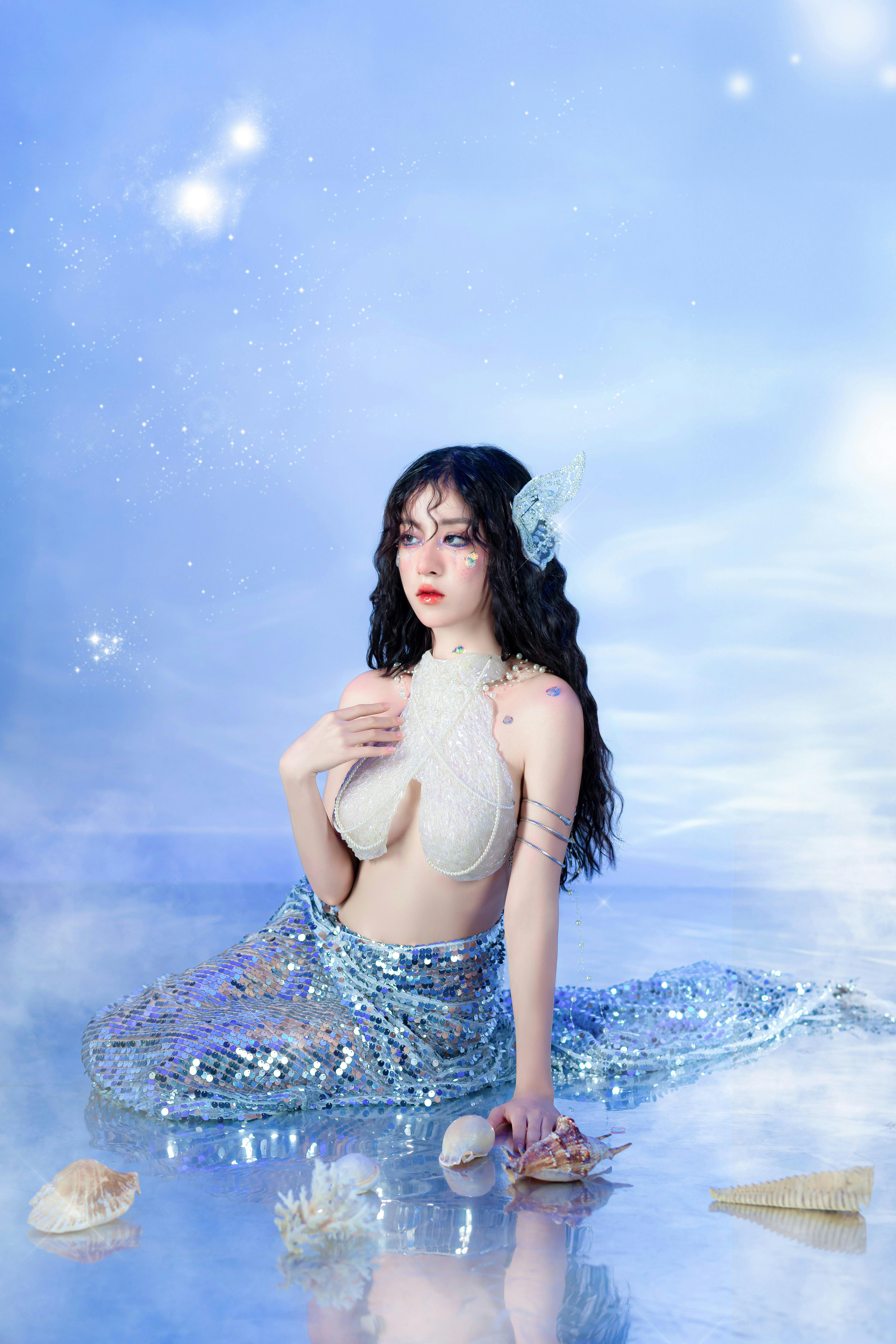 A mystical mermaid sits surrounded by shimmering seashells under a starry sky.
