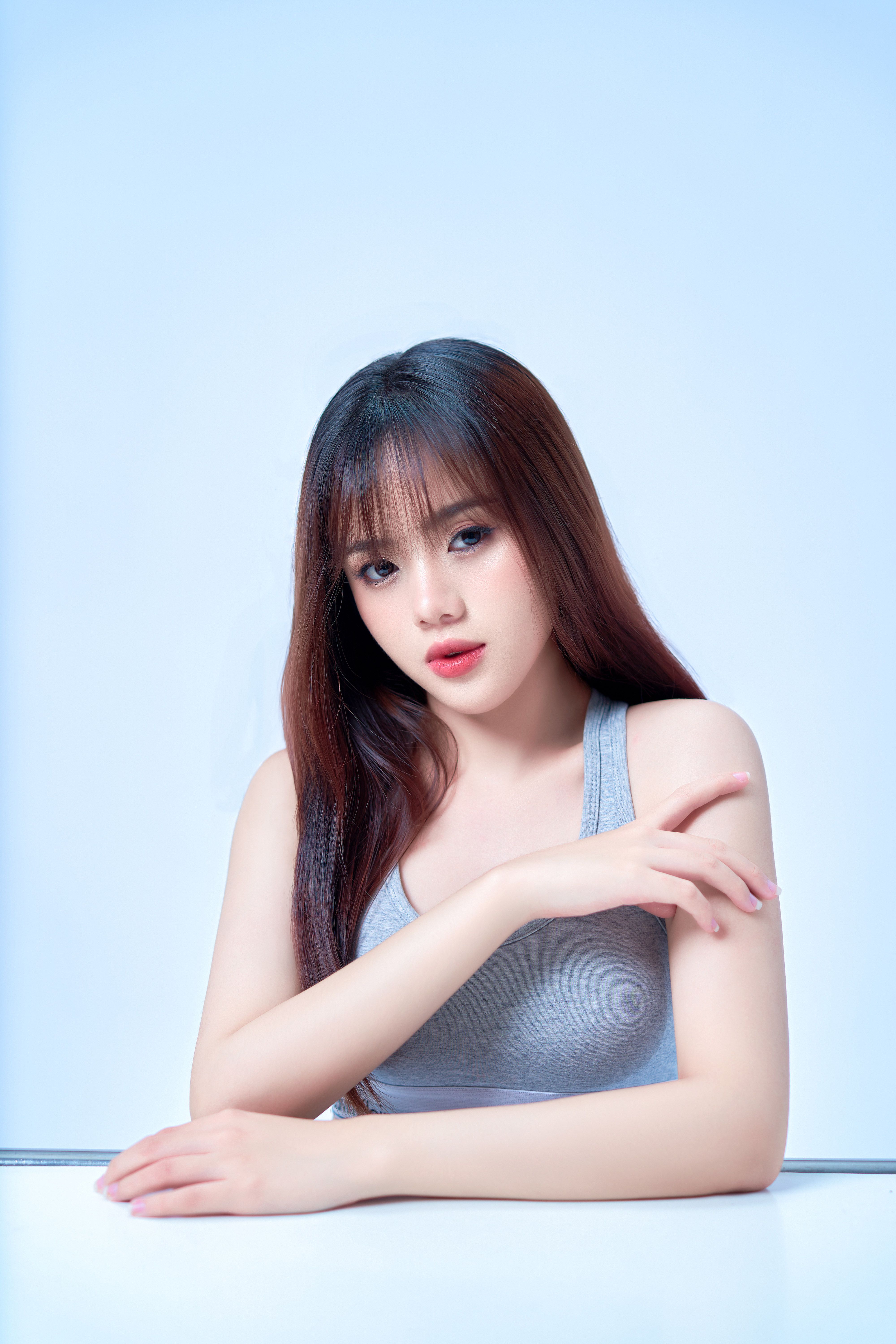 A captivating portrait of a young woman with bangs in a gray tank top against a light background.