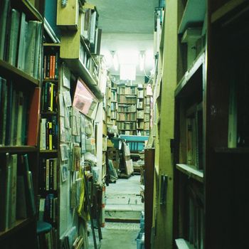 Narrow aisle in a cozy bookshop filled with towering wooden shelves packed with books.（イメージ）