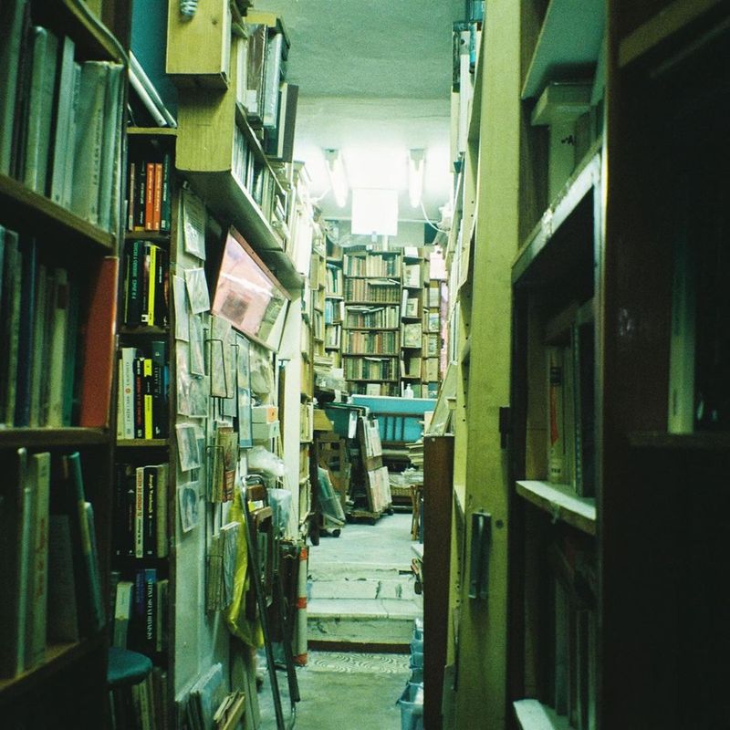 A narrow aisle of a second-hand bookshop lined with full shelves — photo by Kamila  Nguyen on Pexels