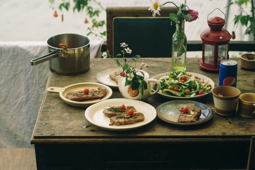 A rustic dining table adorned with meat dishes, fresh salad, and vintage decor, creating a cozy outdoor meal setting.