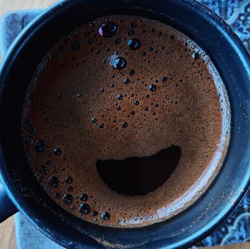 Top view of rich and frothy Turkish coffee in a black mug, creating a smiley face pattern.