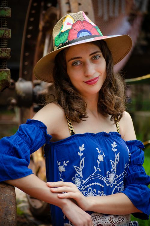 Free Charming woman in a blue embroidered dress and floral hat posing outdoors. Stock Photo