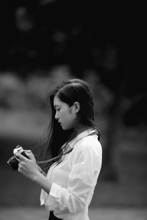 Free A young woman in a black and white setting focuses intently while holding a camera. Stock Photo