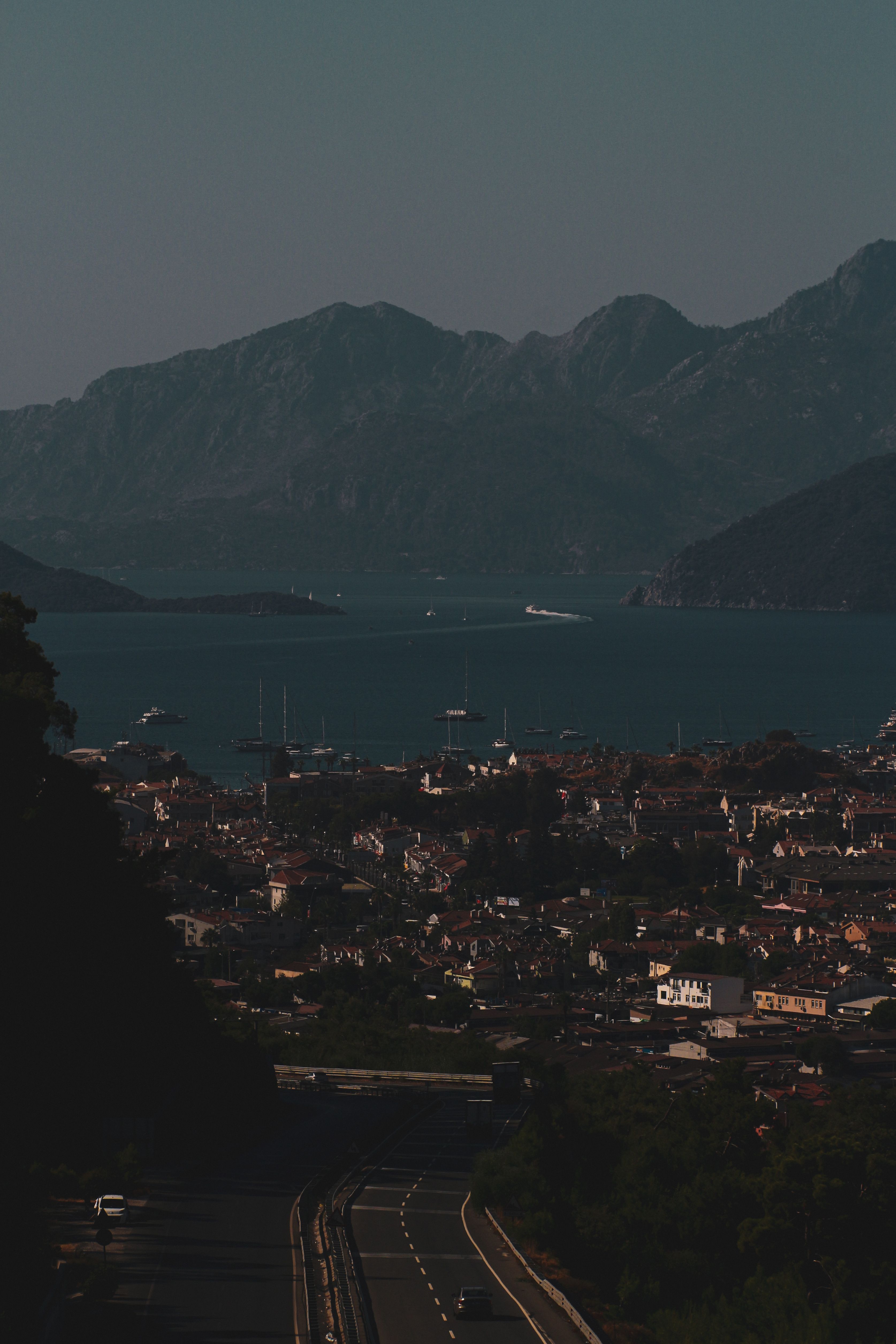 Aerial view of a coastal city nestled between mountains and a bay, under a clear sky.