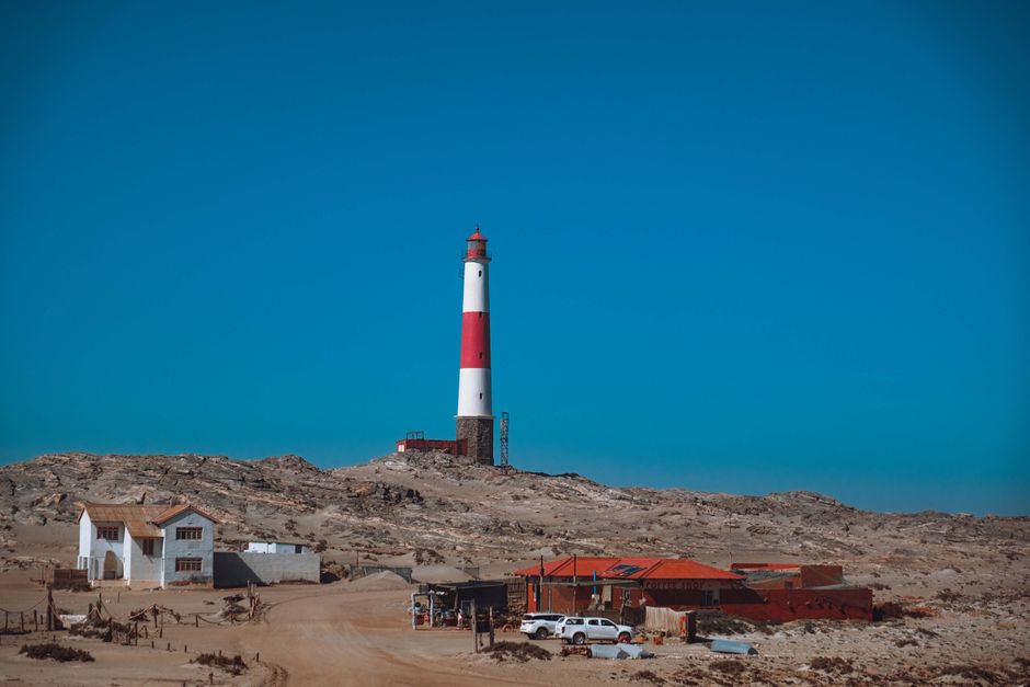 A vibrant red and white lighthouse stands tall on a barren landscape under a clear blue sky, symbolizing safety and guidance.