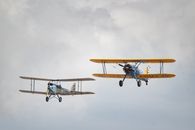 Two vintage biplanes flying in a cloudy sky, showcasing historical aviation.
